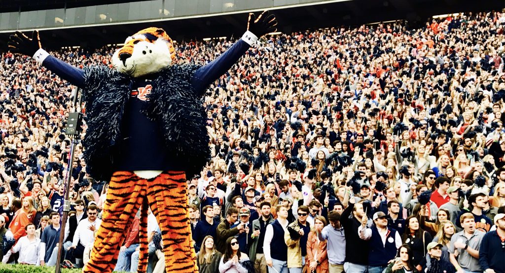 Aubie at Gameday looks out onto the field, with his arms out stretched. Aubie is wearing his navy blue shaker vest and is standing in front of a packed student section.