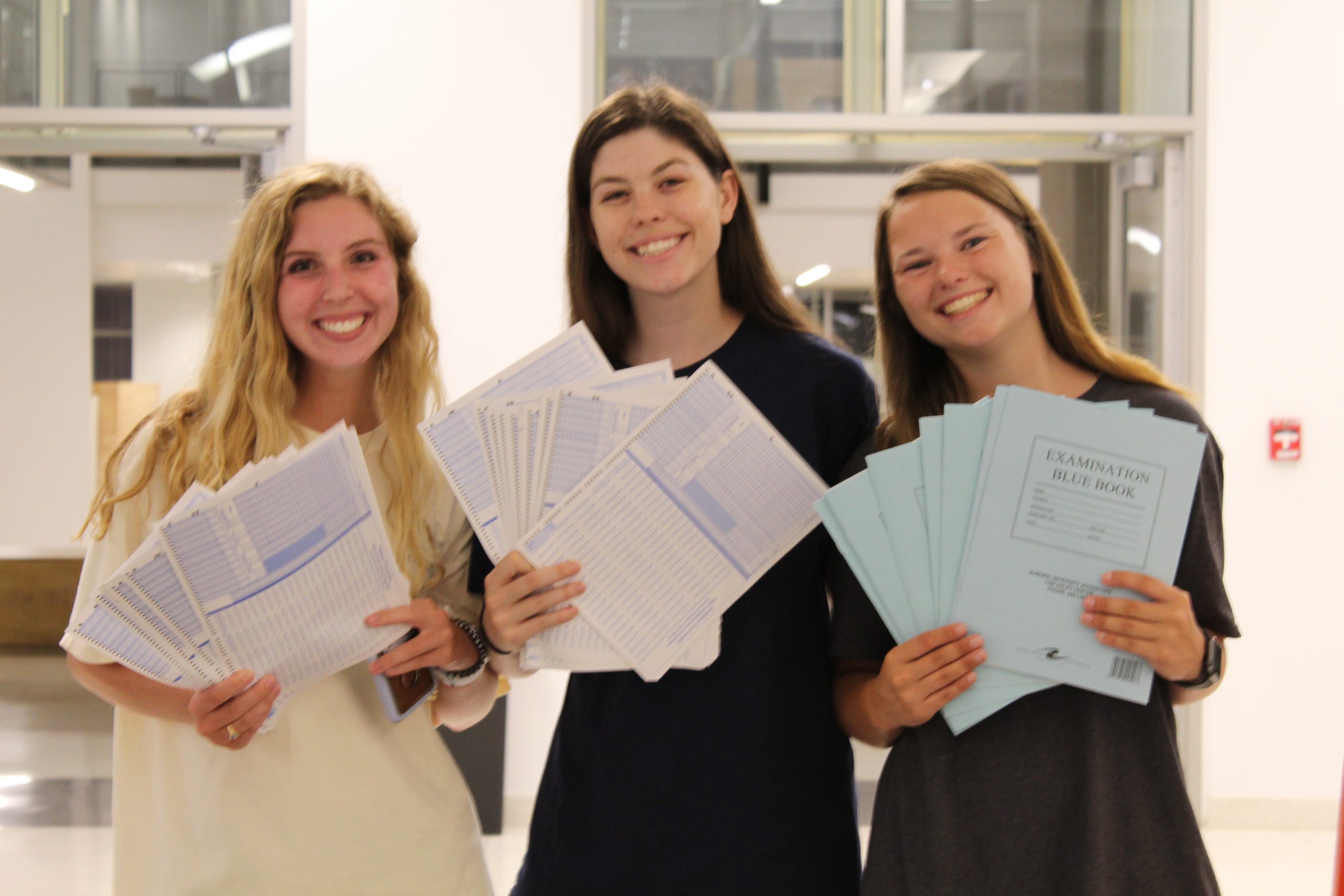 Three Student Government Association members stand in the Mell Classroom Building at a past Up All Night. They are holding scantrons and Blue Books that they passed out to students as they prepare for finals.