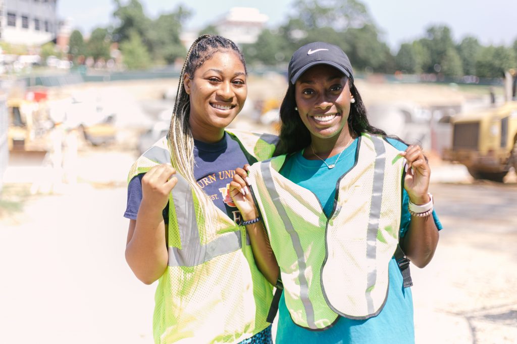 Two Student Government Association members stand in front of a current construction site on campus. They are wearing safety vests to help promote Safety Week.